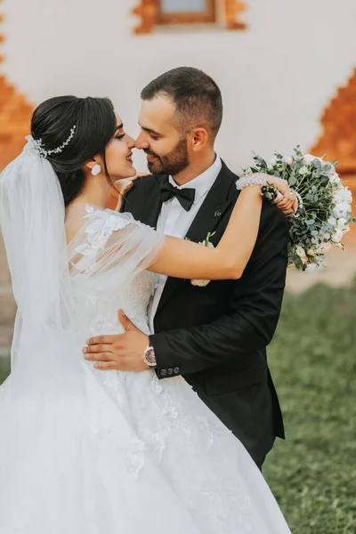 portrait of the bride and groom kissing against the background of the autumn sun of green trees in the garden or park. An incredibly beautiful bride. Stylish groom with a beard