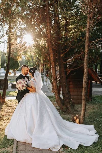 Şık bir gelinlik içinde güzel bir gelin ve damat gün batımında parkta sarılıyor. Büyüleyici genç bir gelin inanılmaz derecede mutlu. Mutlu kız düğün gününde