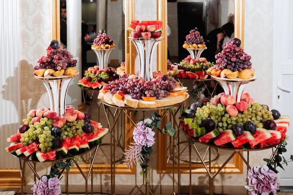 Wedding decorations. Reception. Buffet. Fruits and cheese on plates with bread in boxes. Food bar decorated by flowers and lanters