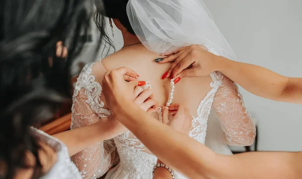 A stylish bride gets dressed with her girlfriends in a hotel room. Morning preparation for the wedding ceremony. Girlfriends help the bride get dressed