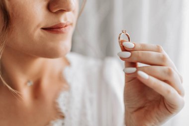 Gelin, parmaklarıyla dudaklarına yakın altın bir yüzük tutuyor, yakın plan. Gelinin sabahı. Düğün günü. Siyah beyaz fotoğraf