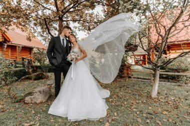 Rüzgarda süzülen duvağı olan zarif, zarif bir gelin. Ve şık bir damat uzun sonbahar ağaçlarının yanında dışarıda öpüşüyor.