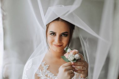 Kadın güzelliği. Evde hoş bir kadın var. Gelin fotoğrafçı için poz veriyor. Şık bir kadın beyaz bir elbise giyer. Profesyonel makyaj ve saç modeli. Gelinin kafasında bir diyabet ve uzun bir peçe var..