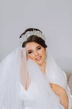 Saçları güzel bir gelin portresi ve başında taç ve odasında beyaz bir bornozla duran doğal makyaj malzemesi. Kızın güzelliği. Uzun beyaz bir peçe.