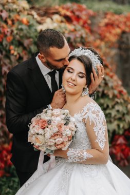 Evin yanındaki sonbahar parkında gelin ve damat, düğün töreni, ön manzara. Sarı sonbahar yapraklarının arka planında damat ve gelin.