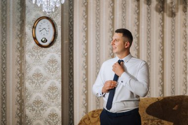 Damat odasında kravatını takar ve düğün için hazırlanır. Adam mavi kravat takıyor.