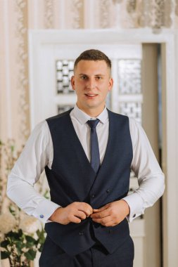 Damat odasında yeleğini giyer ve düğün için hazırlanır. Adam mavi kravat takıyor.