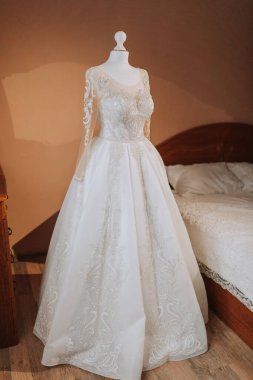 Pahalı bir otelin iç tarafında, iki taraftaki bir pencereden yansıyan doğal ışıkla aydınlatılmış lüks dantelli bir gelinlik.