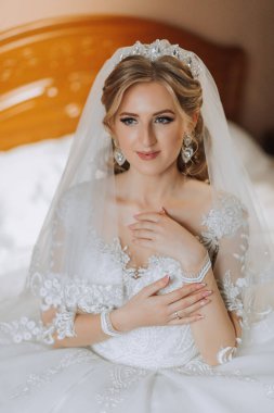 Yatakta oturan neşeli, gelinlikli genç bir gelinin orta sınıf portresi. İçeride poz veren mutlu kız..