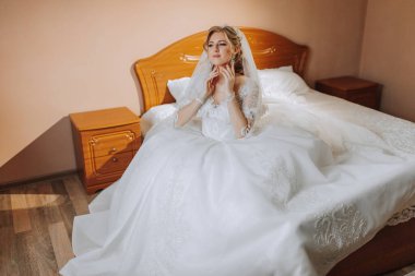 Yatakta oturan neşeli, gelinlikli genç bir gelinin orta sınıf portresi. İçeride poz veren mutlu kız..