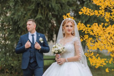 Sonbahar ormanında damat ve gelin, düğün töreni, yan manzara. Sarı sonbahar yapraklarının arka planında damat ve gelin. Fotoğraf ağaçların sararan yapraklarının arasından çekildi.