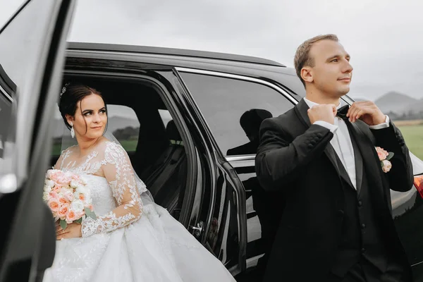 スタイリッシュな結婚式のカップル 秋に車の近くにポーズアップグロム 幸せなロマンチックな若いカップルは結婚を祝います オープン 優しい瞬間だ 花束で花を飾る — ストック写真