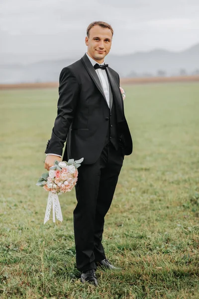Handsome groom in black suit and black bow tie standing outdoors. Wedding portrait. A man in a classic suit