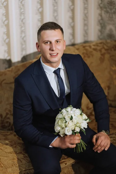 The elegant groom put on a jacket in his room. Details of the wedding morning. Details Beauty and fashion. Groom with a bouquet of flowers