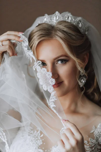 一位漂亮的金发新娘穿着白衣站在她的房间里 看着摄像机 一个快乐女孩的婚纱照 — 图库照片