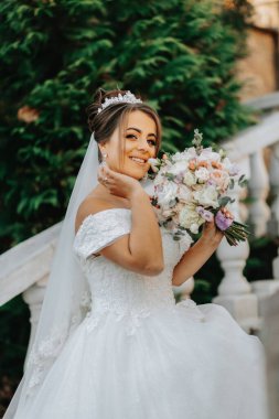 Sonbahar parkında taş basamaklardaki gelinin portresi. Elinde bir buket çiçekle, doğal bir arka planda gelinlik giymiş gelin. Düğün günü..