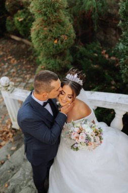 Mutlu düğün çifti portresi, sonbahar ormanında gelin ve damat taş merdivenlerin yanında poz veriyor. Takım elbiseli bir adam, gelinlikli bir kız. Damat kız arkadaşını öpüyor. Yukarıdan Fotoğraf