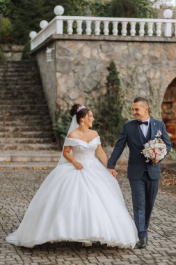 Muhteşem bir düğün çifti parktaki eski şatonun yakınındaki taş merdivenlerde yürüyor. Eski binanın arka planında poz veren muhteşem gelinlik ve damatla şık bir gelin.