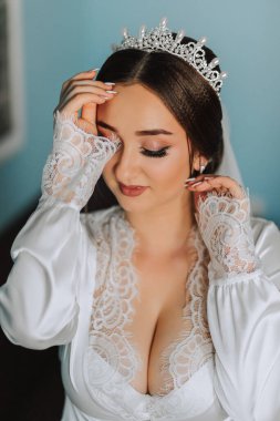 Kafasında taç olan bornozlu bir gelinin harika bir portresi. Güzel bir düğün makyajı, saç stili ve saç aksesuarı. Gelin gülümsemesi, portre