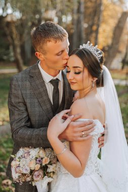 Doğadaki gelin ve damadın portresi, birbirine aşık güzel bir çift. Sonbahar ağacı yaprakları. Yeni evliler sonbahar parkında yürüyorlar.