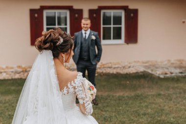 Damat ve gelin parkta uzun yeşil ağaçların arasında el ele tutuşuyorlar. Geniş açılı sonbahar fotoğrafı. Gönüllü gelinlik. Damadın klasik takımı.