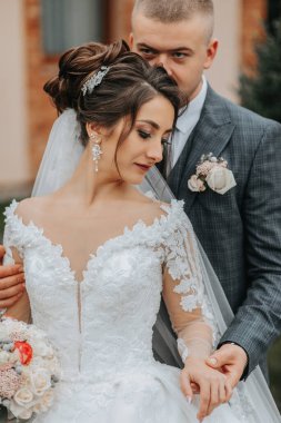 Şık gelin ve damat nazikçe sarılıp öpüşüyor. Güz parkında modern buketli, şık damadı kucaklayan güzel gelin. Duygusal romantik an. Düğün için. Şık ve güzel..