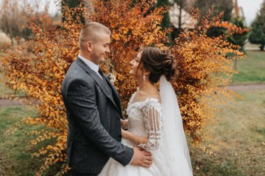Şık gelin ve damat nazikçe sarılıp öpüşüyor. Güz parkında modern buketli, şık damadı kucaklayan güzel gelin. Duygusal romantik an. Düğün için. Şık ve güzel..