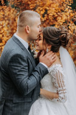 Şık gelin ve damat nazikçe sarılıp öpüşüyor. Güz parkında modern buketli, şık damadı kucaklayan güzel gelin. Duygusal romantik an. Düğün için. Şık ve güzel..