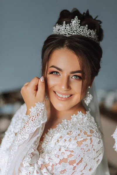 the shy bride covers herself with the sleeves of her lace gown. Portrait of a brunette bride with a tiara on her head and professional make-up