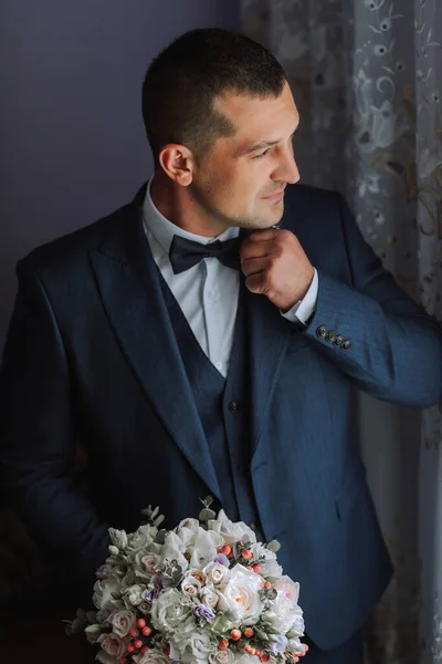 Male portrait. Photo session by the window. Groom\'s collection. The groom puts on a jacket. Wedding photo
