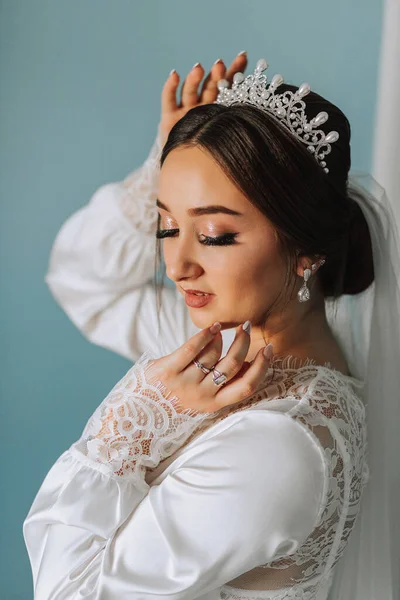 A wonderful portrait of a bride in a robe with a tiara on her head. Beautiful wedding makeup, hairstyle and hair accessories. Bride smiling, portrait