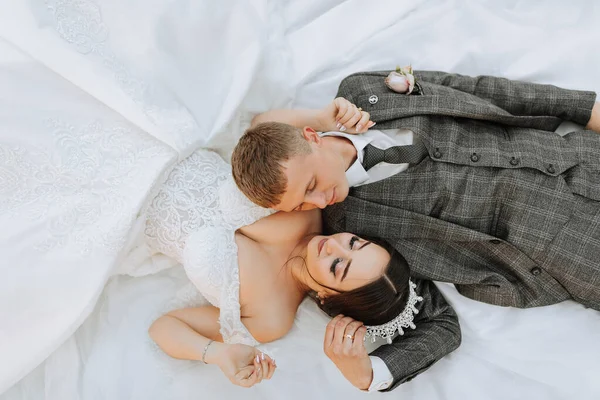 portrait of the bride and groom lying on the grass and kissing. An incredibly beautiful bride. Stylish groom in a suit
