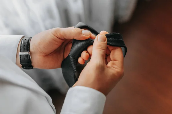 man\'s tie in hands, close-up photo of hands. The groom is preparing for the ceremony