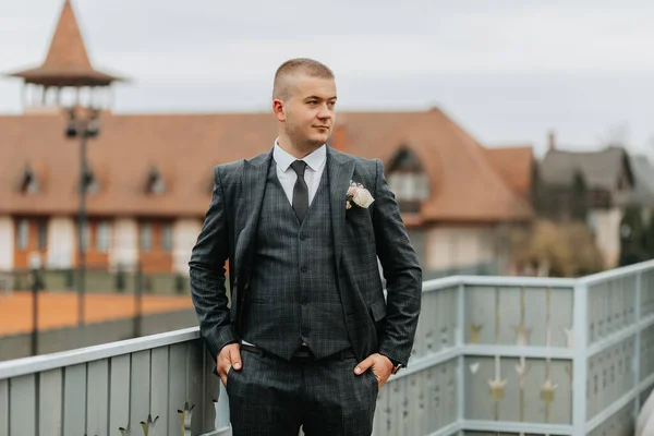 Handsome groom in suit and tie standing on balcony outdoors. Wedding portrait. A man in a classic suit
