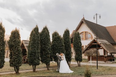 Şık gelin ve damat nazikçe sarılıp öpüşüyor. Güz parkında modern buketli, şık damadı kucaklayan güzel gelin. Duygusal romantik an. Düğün için. Şık ve güzel..