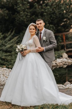 Şık gelin ve damat nazikçe sarılıp öpüşüyor. Güz parkında modern buketli, şık damadı kucaklayan güzel gelin. Duygusal romantik an. Düğün için. Şık ve güzel..