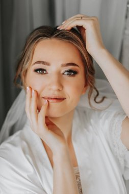 Sabahları beyaz pijamalı güzel ve nazik bir gelin. Güzel doğal makyaj. Düğün saç stili. Gelinin sabahı.