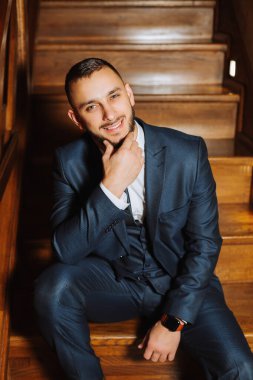 Sakallı, güzel mavi ceketli ve beyaz gömlekli zarif bir damat. Klasik giyinmiş bir iş adamı. Esmer adam ahşap merdivenlerde oturur. Stüdyo resmi