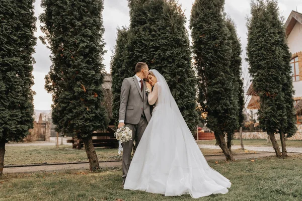 スタイリッシュな花嫁とグロムは優しく抱擁し キスします 秋の公園でスタイリッシュなグロムを取り入れたモダンなブーケで美しい花嫁 感動的なロマンチックな瞬間 ウェディング スタイリッシュで美しい — ストック写真