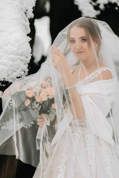 A close-up winter wedding portrait of a beautiful bride under a veil. Sweet and happy girl, bride. A stunning young bride is incredibly happy.