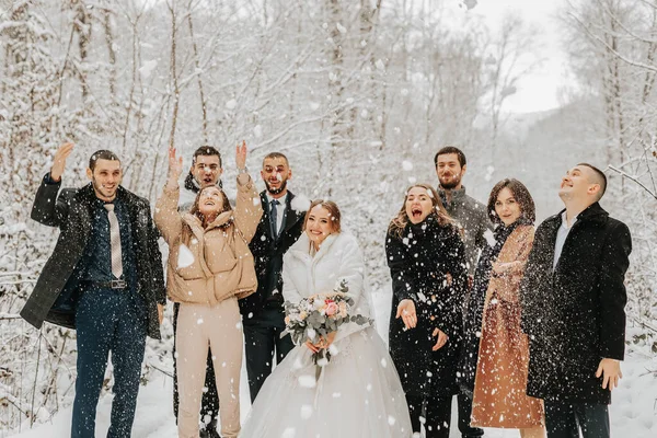 A group of young people, friends of the bride and groom, throw snowballs together with the bride and groom in a fairy-tale snowy forest