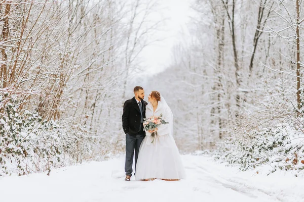 冬の雪の森で歩く美しい結婚式のカップル 白いドレスとミンク毛皮のコートの女性 黒いコートのひげ付き男性 — ストック写真