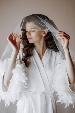 Güzel, genç bir gelin, yakın plan, uzun kıvırcık saçlı, yüzünü bir peçeyle örtüyor. Profesyonel saç ve makyaj.