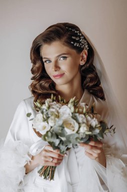 Uzun kıvırcık saçlı, şık beyaz cüppeli güzel bir gelin elinde bir buket çiçek tutuyor. Sabahları beyaz elbiseli güzel bir genç kız. Düğün hazırlıkları.