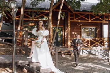 Beyaz bir gelinlik içinde uzun kıvırcık saçlı, açık havada elinde bir buket çiçekle mutlu bir genç kadın. Çiçekli güzel kız. Dikey fotoğraf