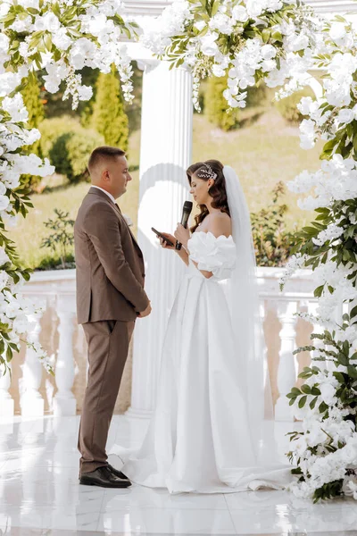 sensitive ceremony of the bride and groom. A happy newlywed couple is standing against the background of a wedding arch, she says yes to him. Wedding vows. The emotional part of the wedding
