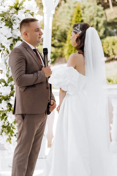 sensitive ceremony of the bride and groom. A happy newlywed couple is standing against the background of a wedding arch, she says yes to him. Wedding vows. The emotional part of the wedding