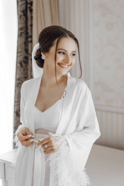 Beyaz cüppeli, profesyonel saç stili ve doğal makyajlı gelin kızın portresi otel odasında muhteşem bir iç mekanı var.