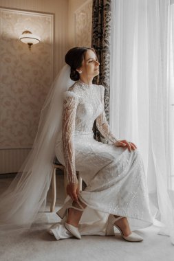 Arap tarzı dantelli ve kristalli lüks gelinlik içinde güzel bir gelinin moda portresi. Güzel gelin ayakkabılarını giyer. Düğün hazırlıkları..