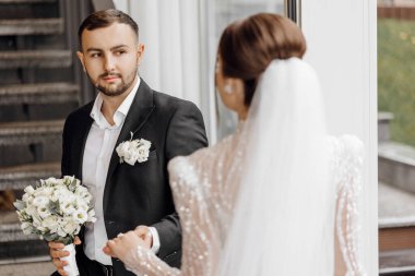 Yakışıklı bir adam gelinin elini nazikçe tutar ve ona sevgiyle bakar. Düğün konsepti. Damat nazikçe geline dokunur.